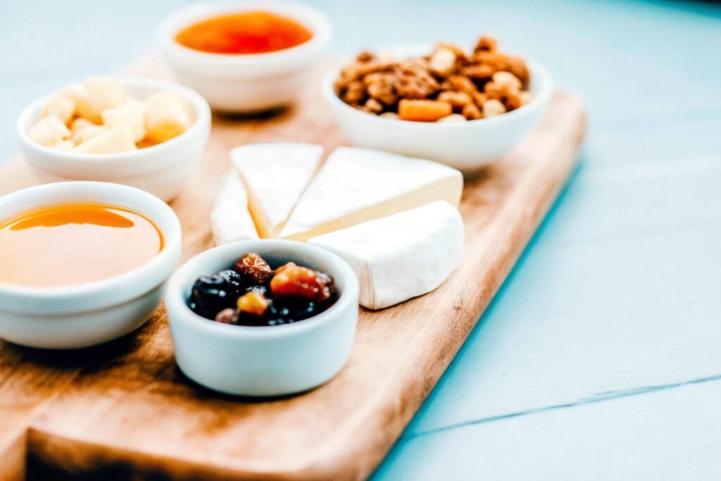 Ingredients for Brie Cheese Bites including brie cheese, puff pastry, honey, nuts, jam, and fresh herbs, arranged on a rustic wooden table