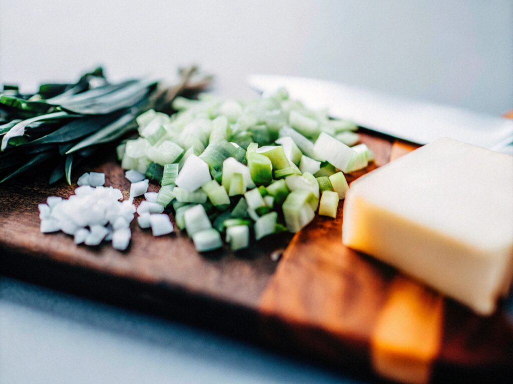 A close-up of diced celery, onions, and fresh sage on a wooden cutting board next to a stick of butter