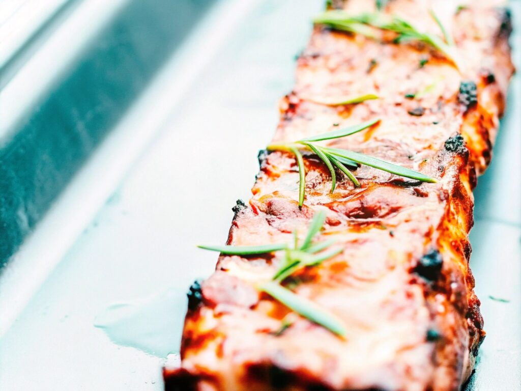 Juicy grilled boneless short ribs on a barbecue with charred edges and garnished with fresh rosemary