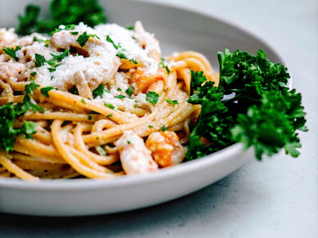 A close-up photo of creamy chicken and shrimp carbonara served on a white plate, garnished with fresh parsley and grated Parmesan cheese