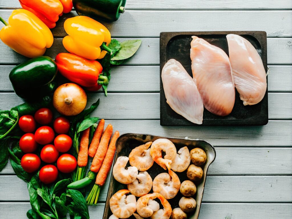 resh chicken breasts, raw shrimp, and an assortment of colorful vegetables arranged on a rustic wooden table