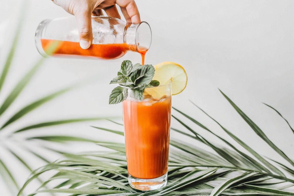 A person pouring fresh carrot juice from a blender into a tall glass, highlighting the easy steps of a homemade carrot juice recipe