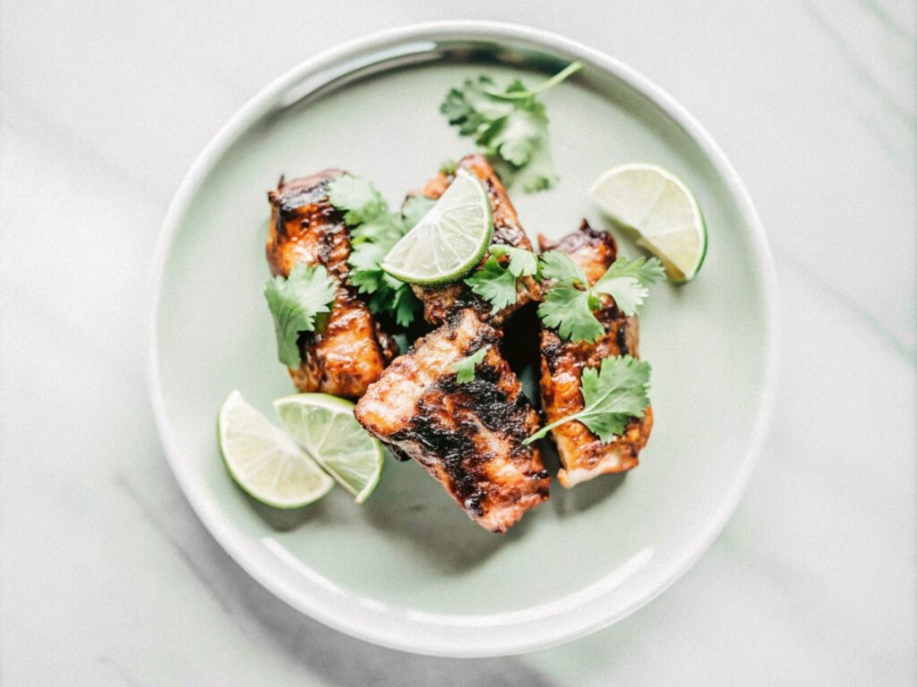 Sweet and spicy glazed boneless short ribs garnished with fresh cilantro and lime wedges on a ceramic plate