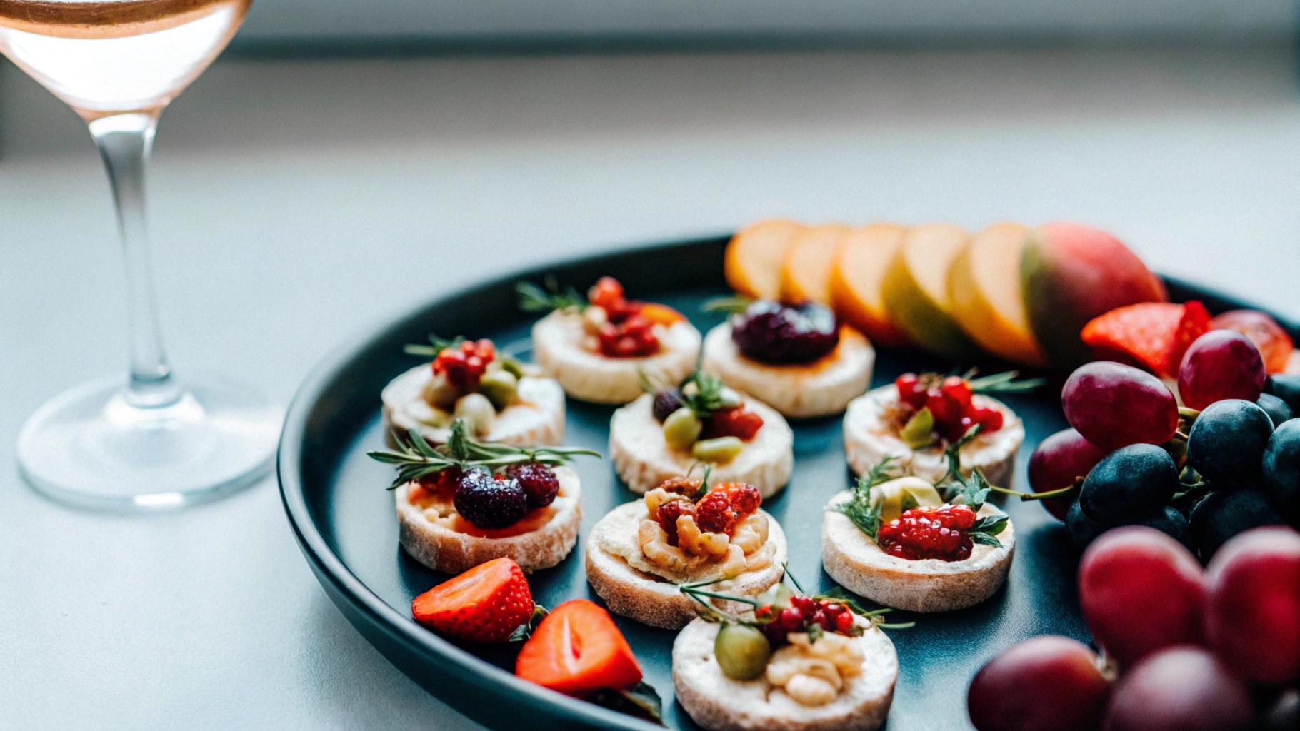 A platter featuring assorted Brie Cheese Bites topped with cranberry sauce, honey, and herbs, served alongside fresh fruits, nuts, and a glass of wine