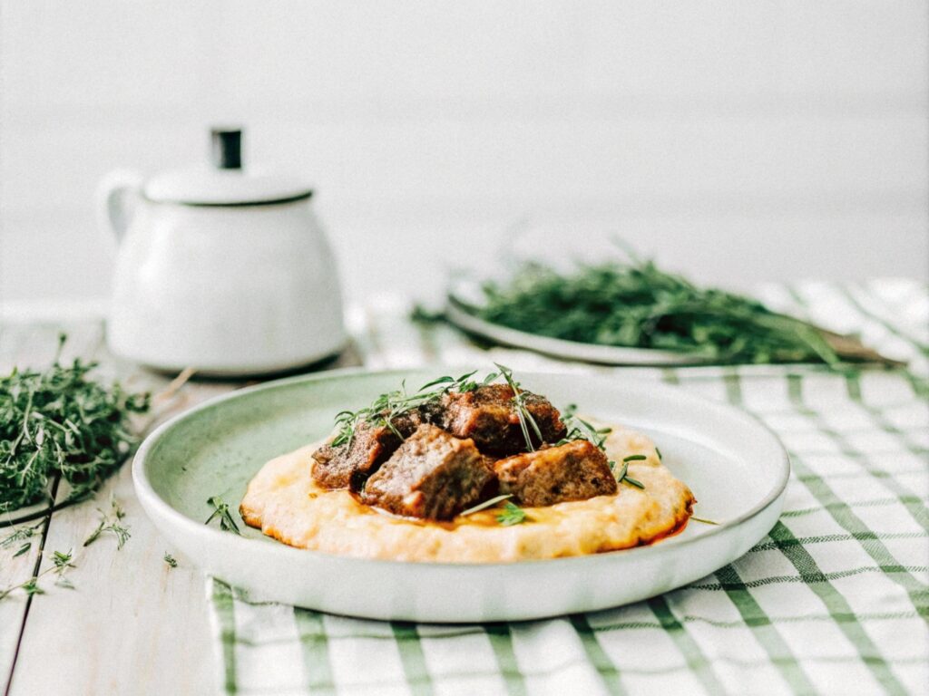 A reheated portion of braised boneless short ribs served over creamy polenta and garnished with fresh thyme