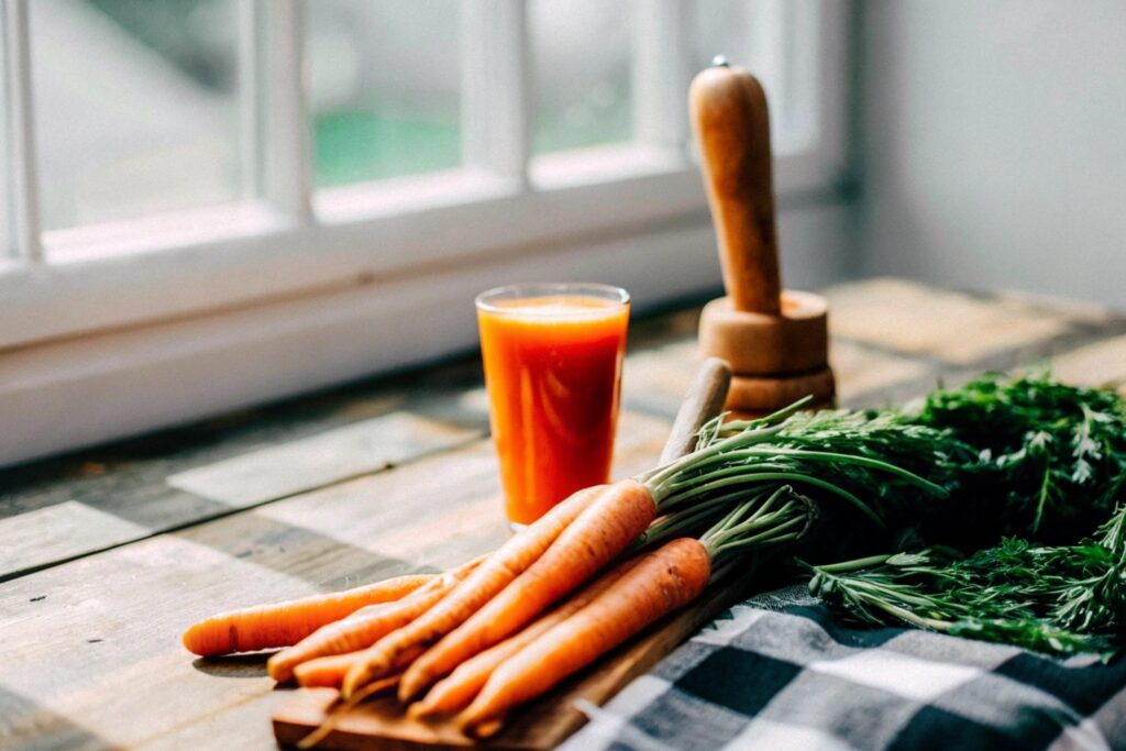 A rustic table displaying carrots, a wooden juicer, and a glass of vibrant carrot juice, symbolizing the global appreciation for carrot juice recipes