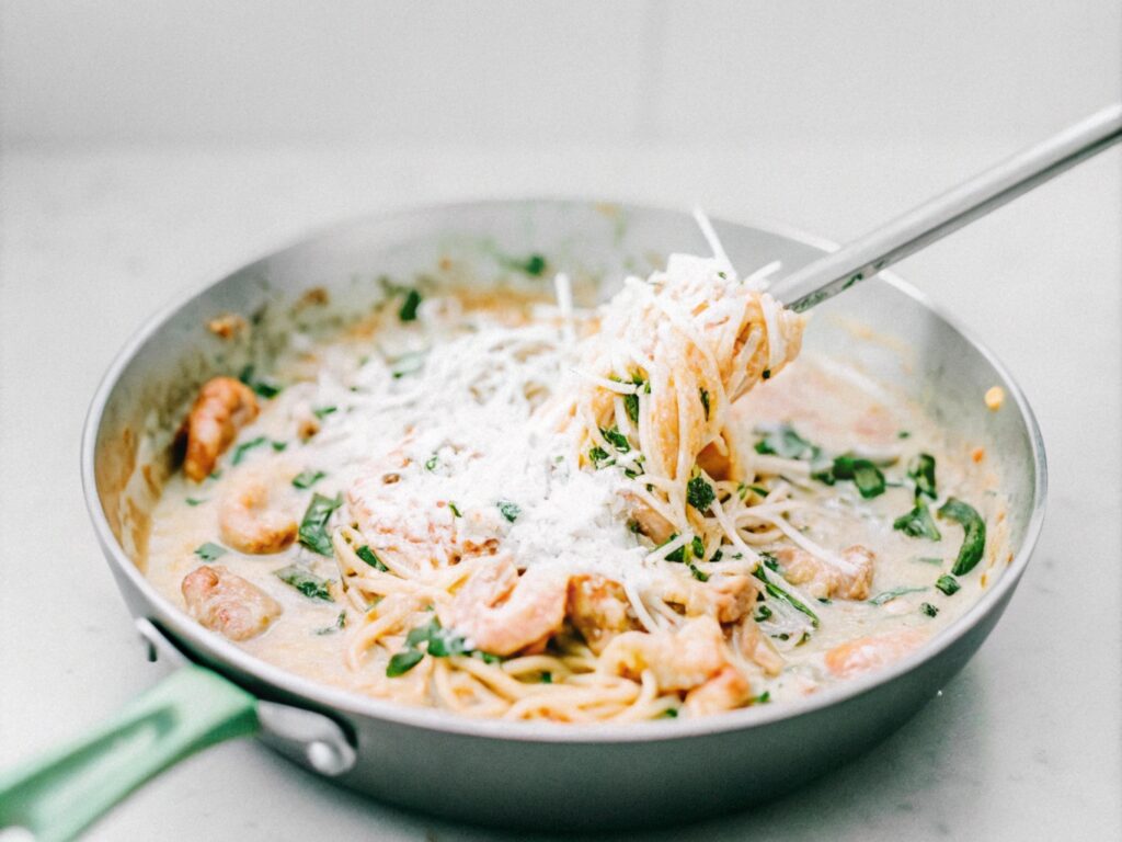 A skillet with creamy chicken and shrimp carbonara being tossed together, with Parmesan melting into the sauce