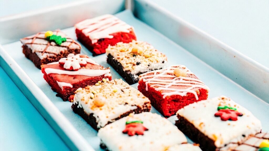 A tray of assorted red velvet brownies featuring holiday decorations, nuts, and white chocolate drizzle for variety