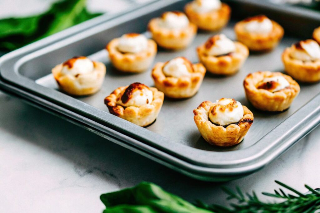 A baking tray filled with golden, freshly baked Brie Cheese Bites, their puff pastry shells glistening under soft lighting