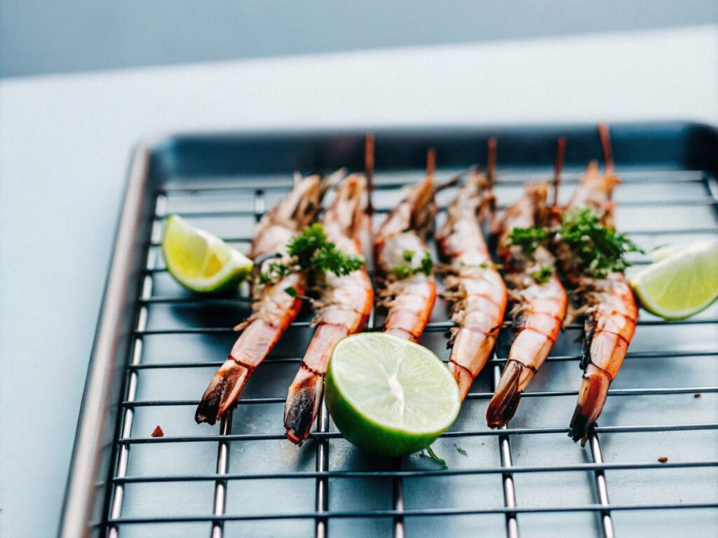 Fresh shrimp on a grill with shells slightly charred, garnished with lime wedges and herbs