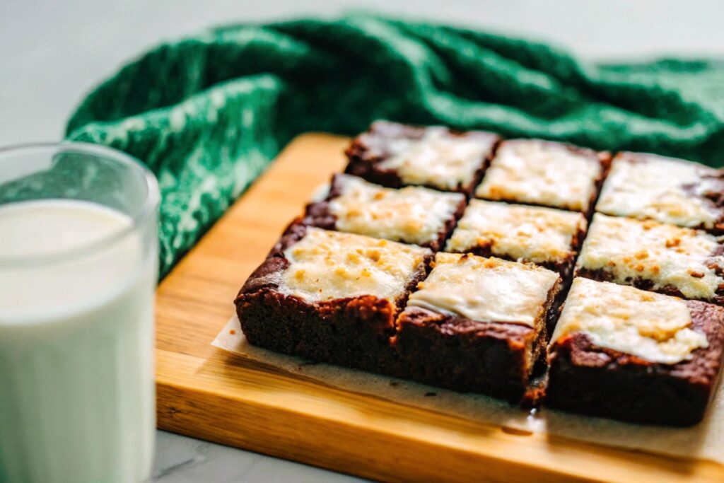 Freshly baked red velvet brownies, cut into neat squares, displayed on a wooden cutting board with a glass of milk beside them