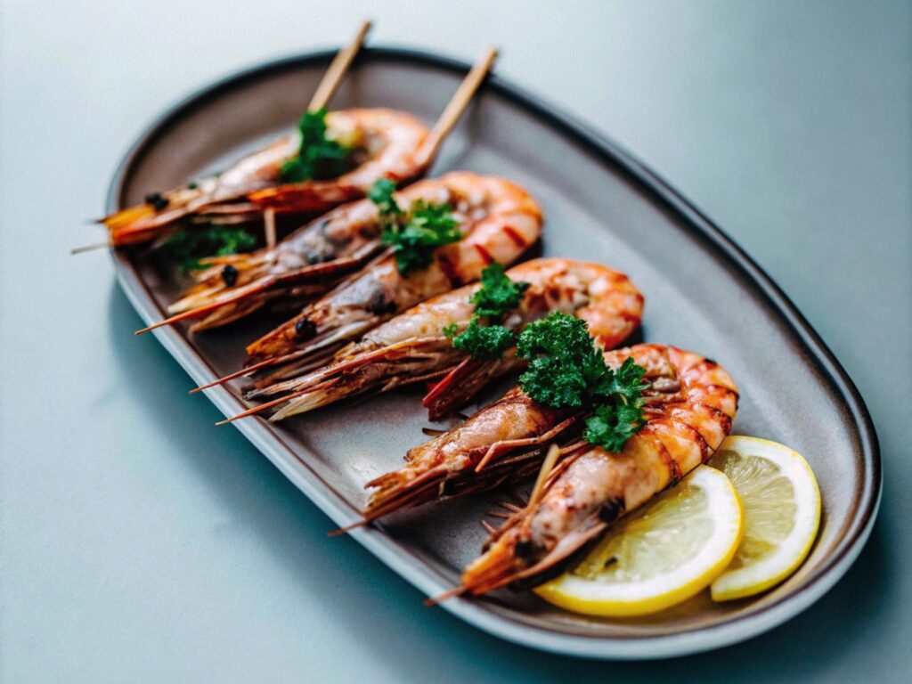 Shell-on grilled shrimp on a serving platter, garnished with lemon slices and fresh parsley.