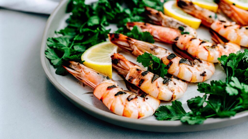 Grilled shrimp with shell-on, served on a platter with lemon slices and fresh parsley garnish