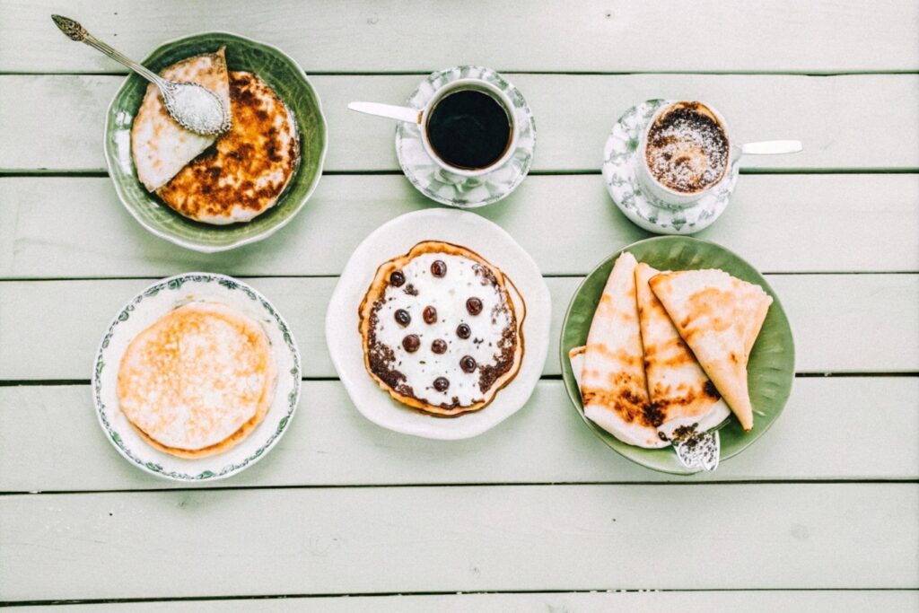 Different styles of hotcakes, including American-style, Japanese soufflé pancakes, and thin French crepes, arranged on a rustic table