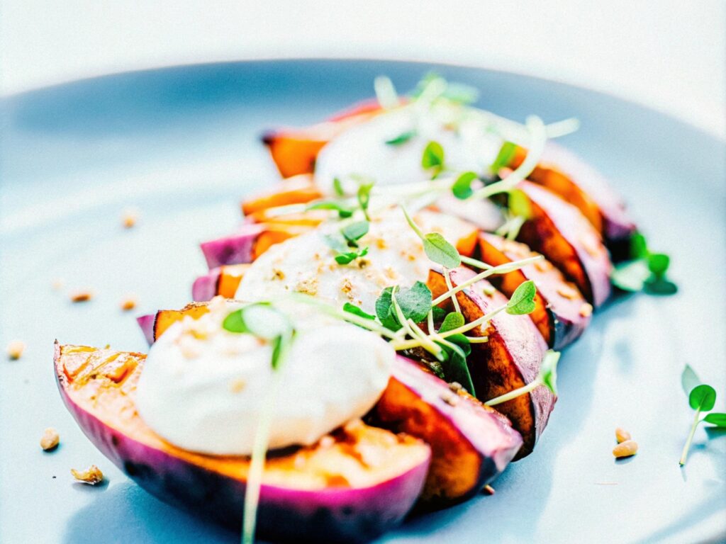 A sophisticated dish of roasted purple sweet potato slices, artfully garnished with delicate microgreens and a creamy dollop of sour cream, showcasing a balanced mix of textures and colors