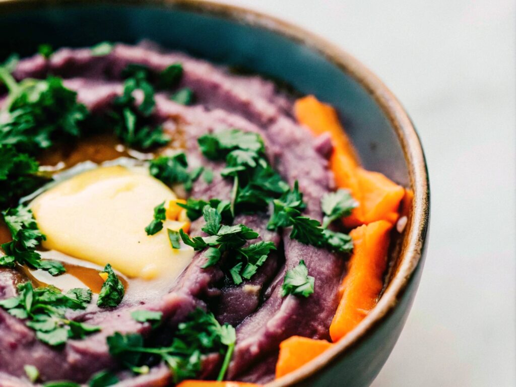 A bowl of velvety mashed purple sweet potatoes, topped with fresh parsley and a melting pat of butter, exuding warmth and creaminess