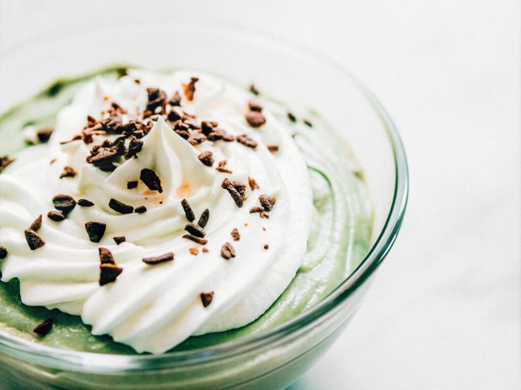 A glass bowl of rich chocolate cottage cheese mousse, garnished with whipped cream and dark chocolate shavings