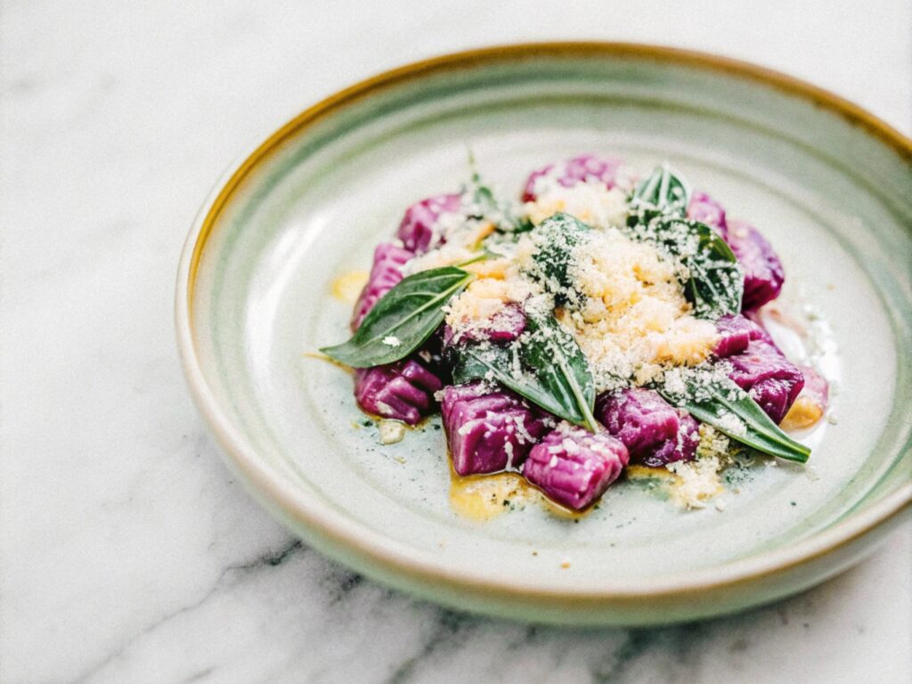 A plate of vibrant purple sweet potato gnocchi, elegantly arranged, garnished with fresh sage leaves, and dusted with parmesan cheese