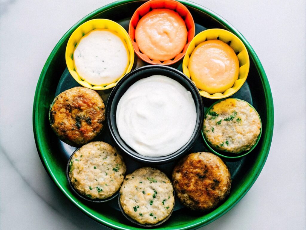 A colorful platter displaying different types of salmon patties, including mini patties, herb-infused patties, and spicy Cajun patties, surrounded by dipping sauces.