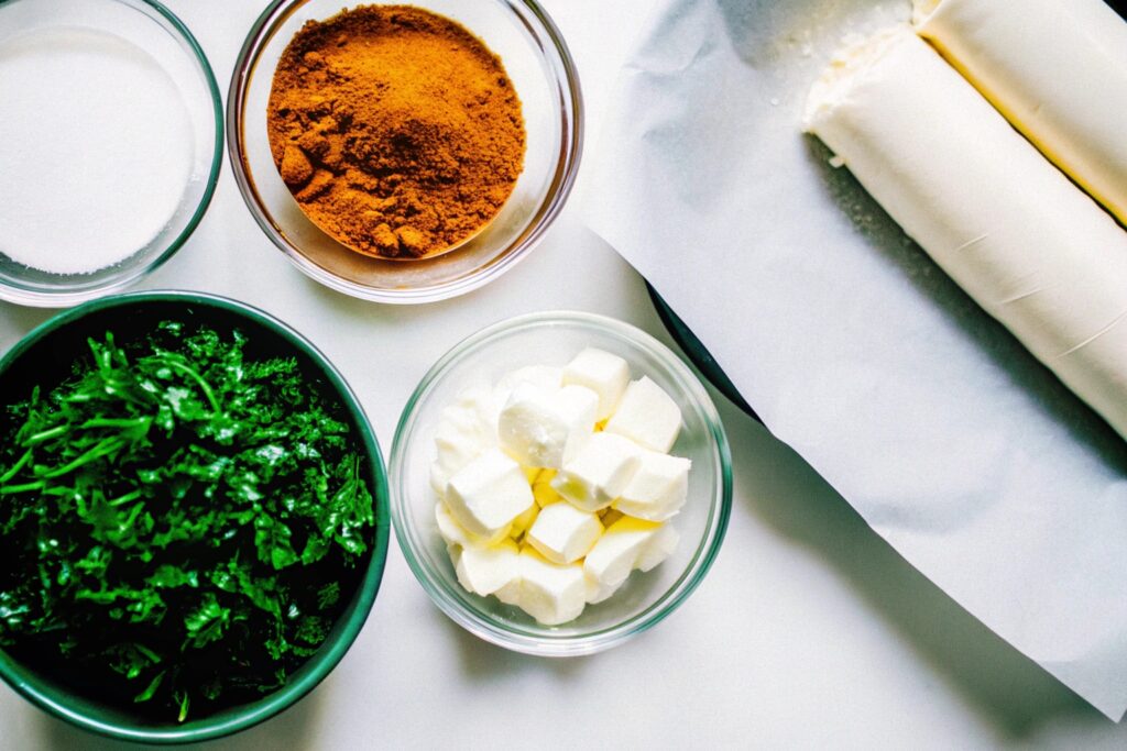 Flat-lay of ingredients for churro cheesecake, including crescent roll dough, cream cheese, sugar, cinnamon, butter, and measuring spoons on a wooden countertop.