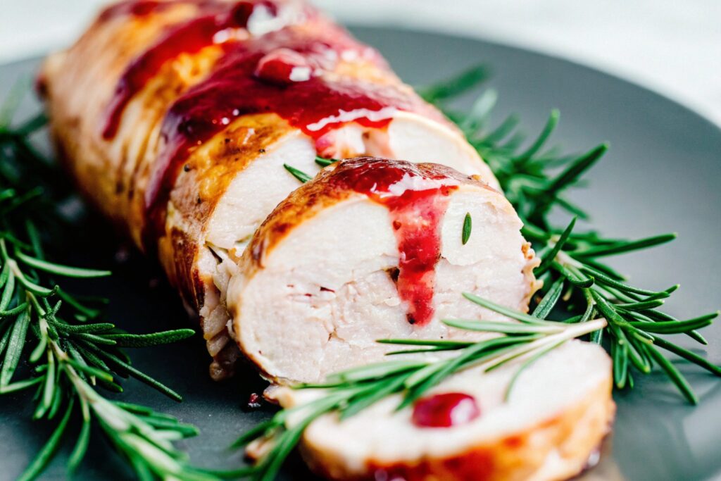 Roasted pork tenderloin drizzled with cranberry sauce glaze, garnished with rosemary sprigs on a serving plate