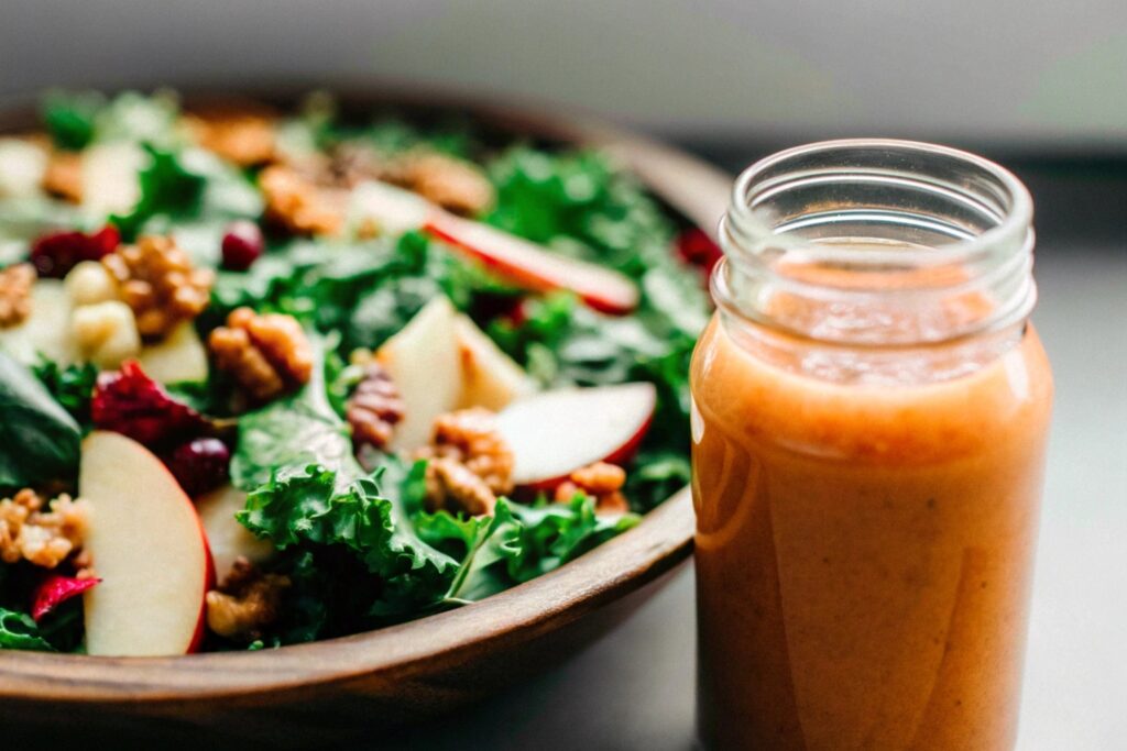 A mason jar of cranberry vinaigrette beside a fresh salad with greens, apple slices, and candied nuts