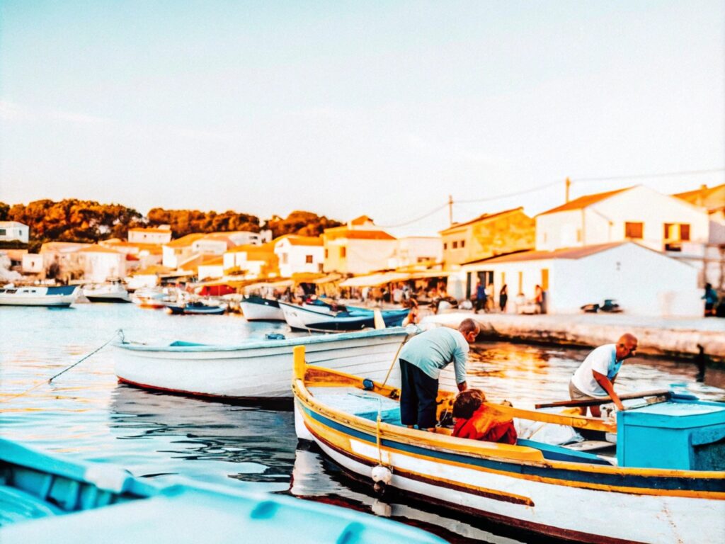 A Mediterranean coastal village at sunrise with fishermen unloading fresh branzino from wooden boats on the shore