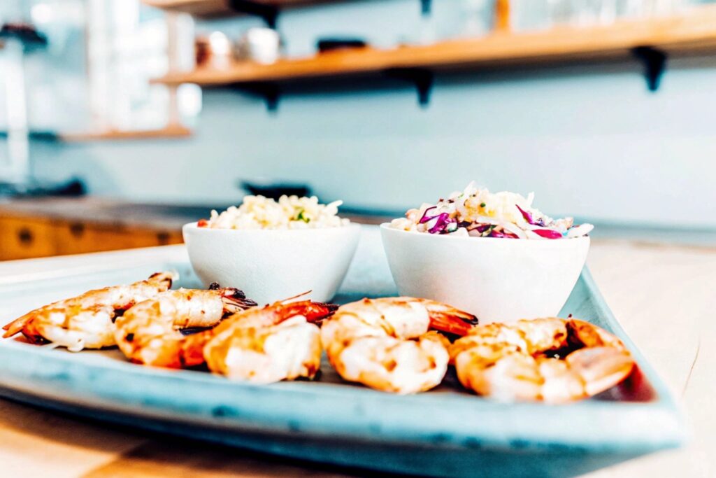 Rustic kitchen scene with a serving platter of grilled shrimp alongside bowls of coleslaw and garlic butter rice