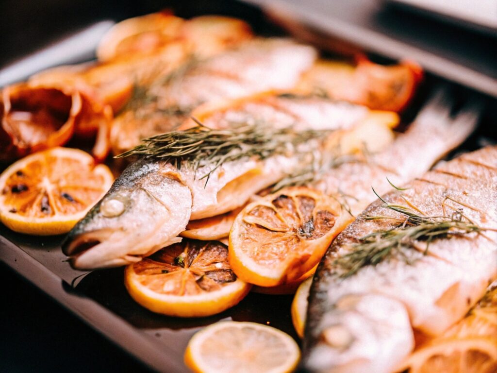 Grilled branzino served on a platter with roasted fennel, citrus slices, and a garnish of fresh herbs