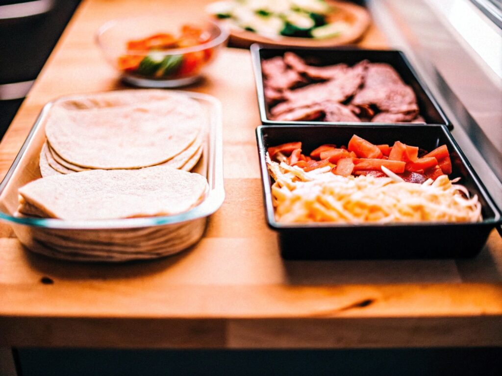 Ingredients for steak quesadilla neatly arranged on a wooden countertop, including steak, tortillas, shredded cheese, and fresh vegetables