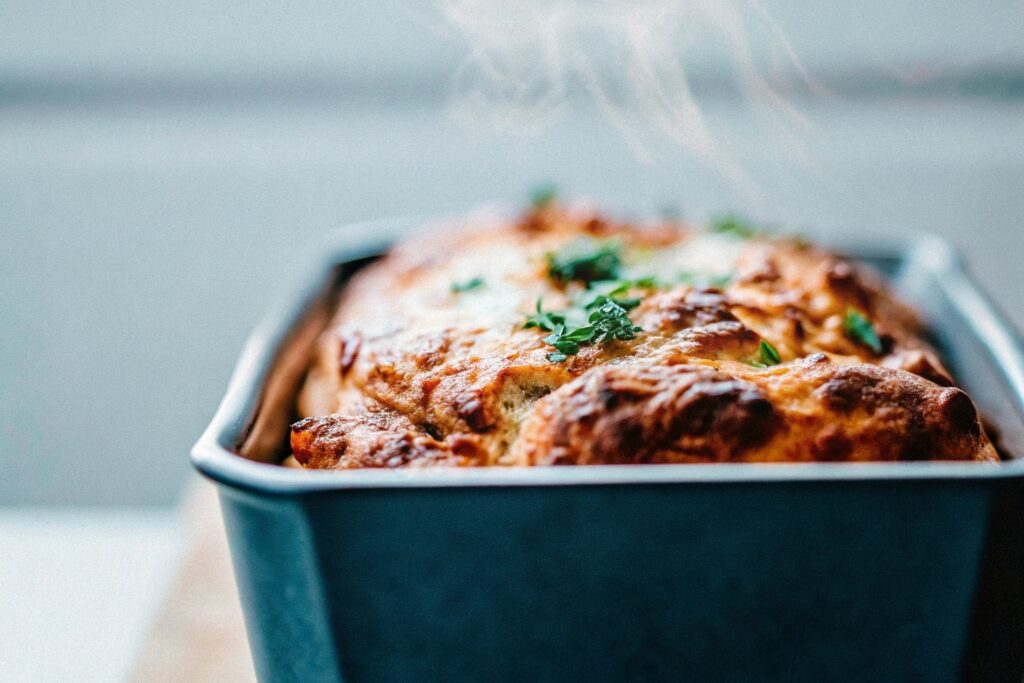 A baking dish with a half-covered chicken casserole inside an oven, with steam escaping from the foil