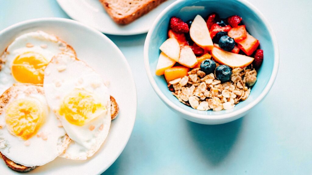 A breakfast spread with scrambled eggs, whole-grain toast, fruit salad, and granola with yogurt.