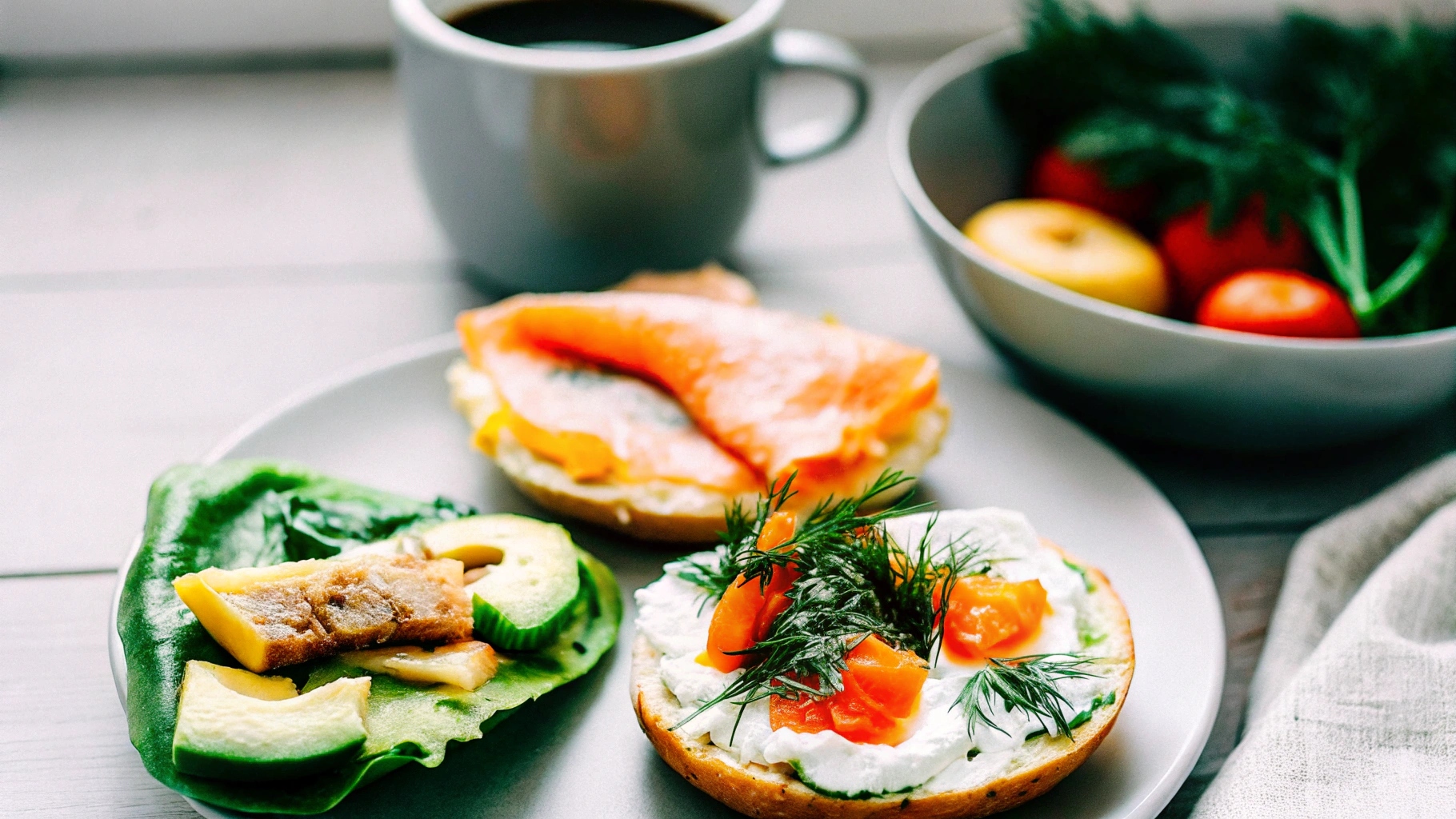 A vibrant breakfast spread showcasing a smoked salmon bagel with cream cheese and dill, a salmon and spinach omelet, a sliced salmon breakfast burrito, and a bowl of fresh fruit, placed on a rustic wooden table with a cup of coffee.