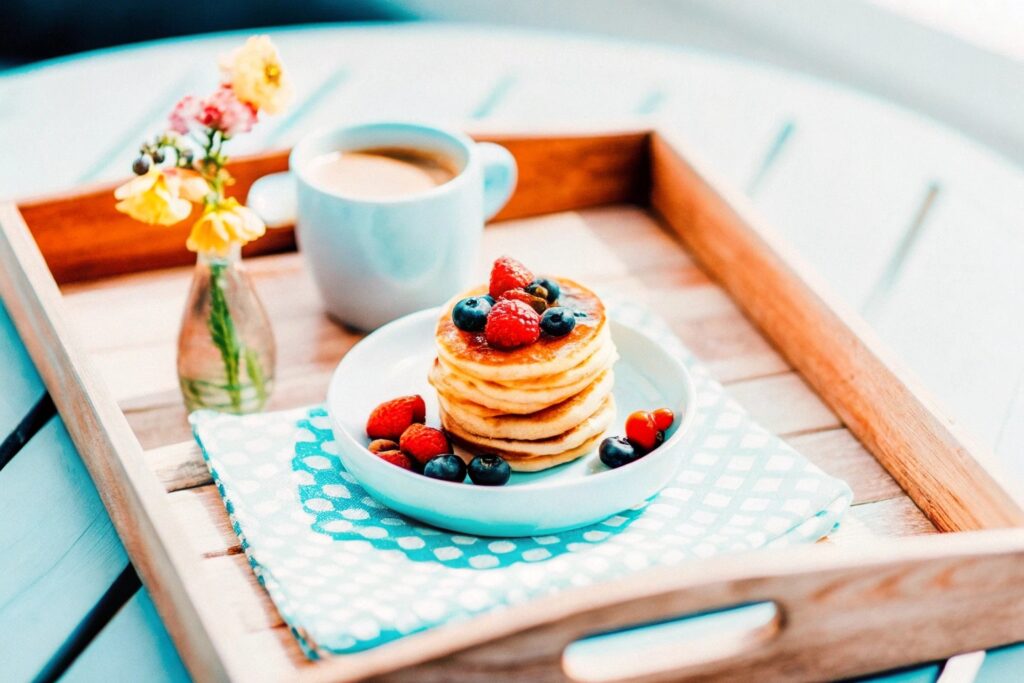 A happy couple sharing breakfast in bed with heart-shaped pancakes and fresh flowers on the tray, sunlight streaming in through the window