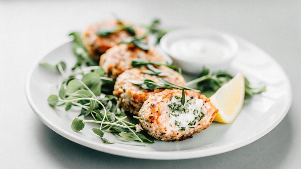 A beautifully plated serving of salmon patties with a crisp golden crust, garnished with fresh parsley and lemon wedges, served alongside a creamy dipping sauce