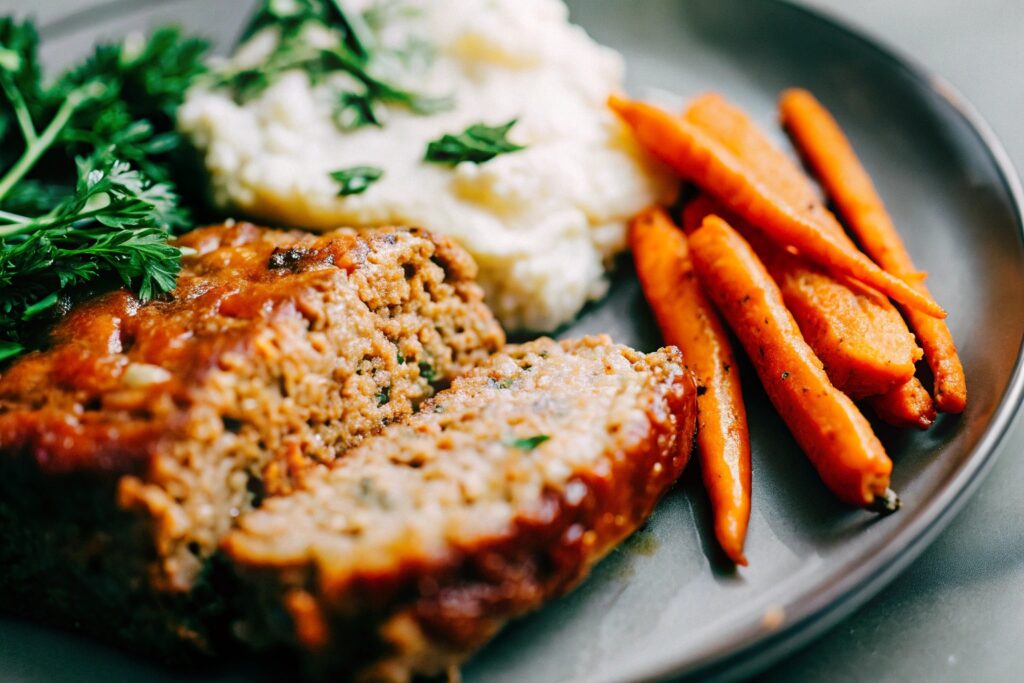 A beautifully plated slice of meatloaf served with mashed potatoes, roasted carrots, and a garnish of fresh parsley