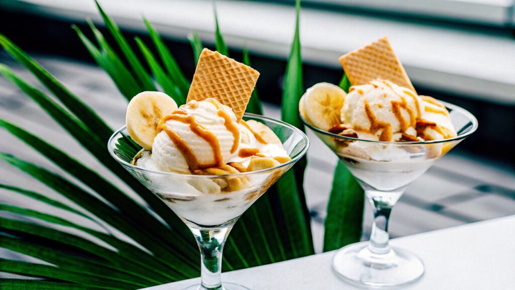 Beautifully styled banana pudding ice cream served in elegant bowls, topped with fresh banana slices, vanilla wafers, and caramel drizzle on a sunny outdoor table