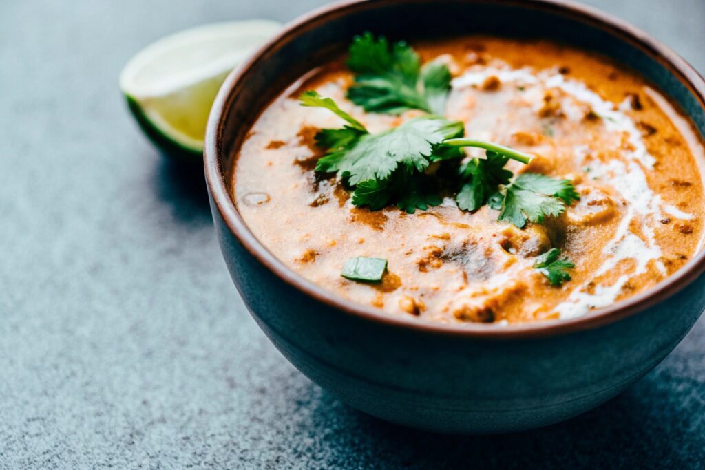 A bowl of creamy El Salvadoran corn soup garnished with cilantro and a side of lime wedges