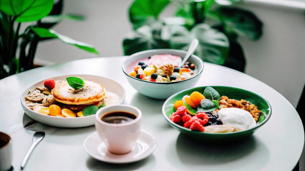 A breakfast table filled with various dessert-inspired breakfasts, including pancakes, parfaits, and smoothie bowls, alongside a cup of coffee