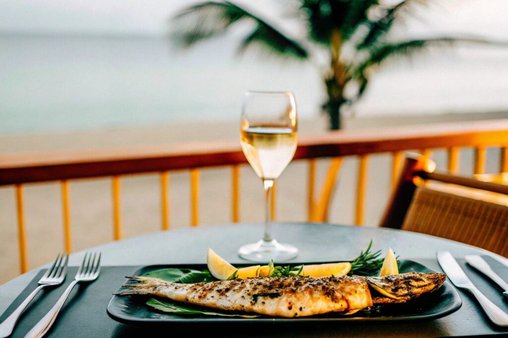 A chilled glass of water beside a grilled branzino served with lemon wedges and herbs, set on a seaside dining table