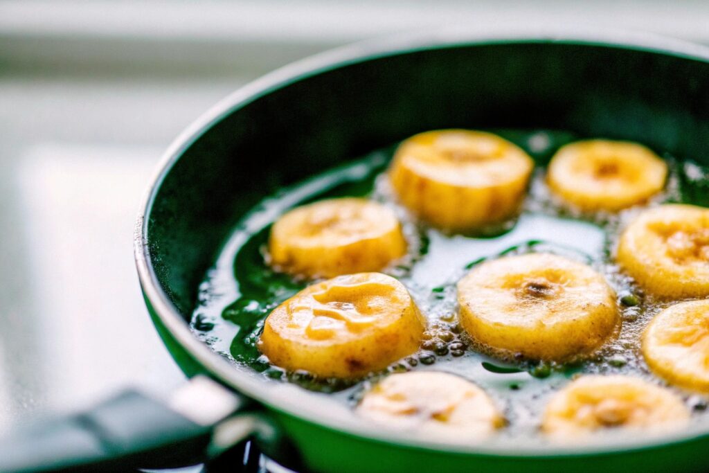 Golden banana slices sizzling in hot oil inside a skillet, with small bubbles forming around the edges