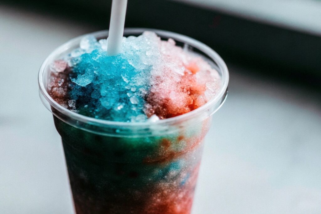 Close-up of a colorful slushy with tiny ice crystals and a straw in a clear plastic cup
