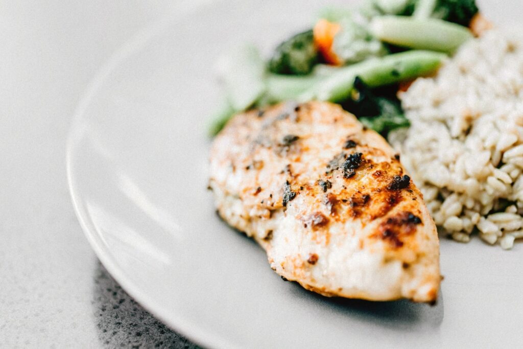 Grilled chicken breast served with steamed vegetables and brown rice on a white plate