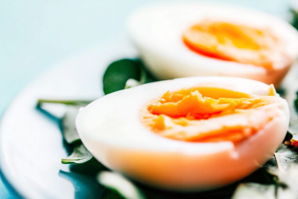 A close-up of a halved boiled egg with a bright yellow yolk, placed on a bed of fresh leafy greens for a nutritious breakfast