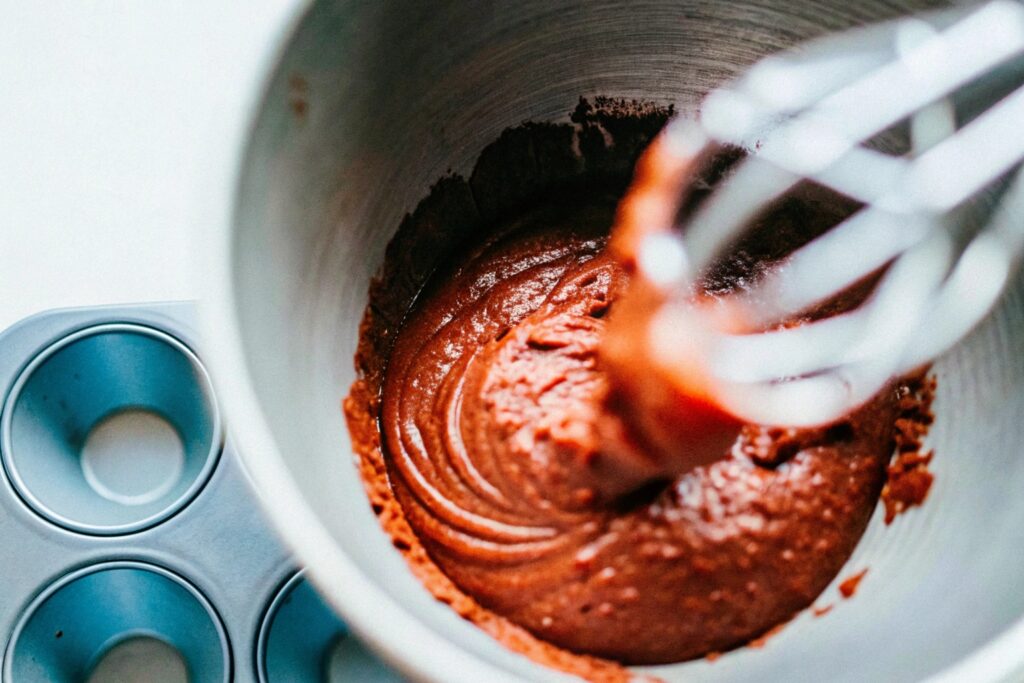 A close-up of a mixing bowl containing red velvet batter, highlighting the vibrant red achieved through food coloring and cocoa powder