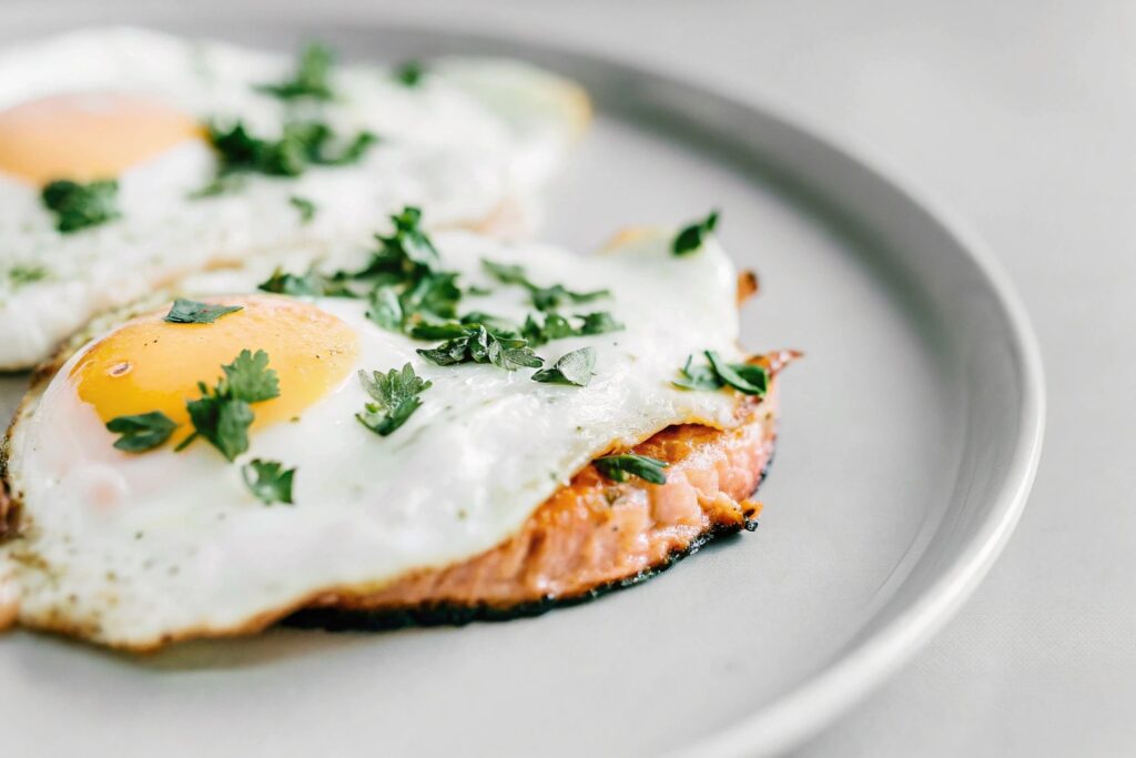 Grilled salmon fillet with sunny-side-up eggs and fresh parsley garnish on a breakfast plate.