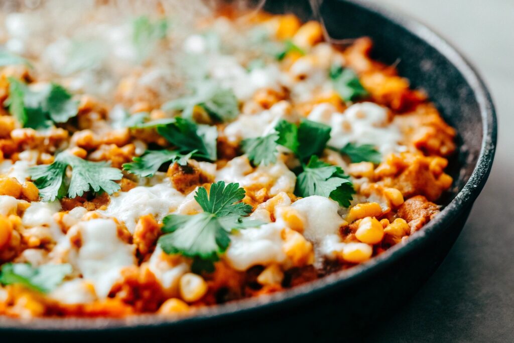 A close-up of the dish in a skillet, steam rising, with vibrant corn, chicken, and melted cotija cheese garnished with fresh cilantro.