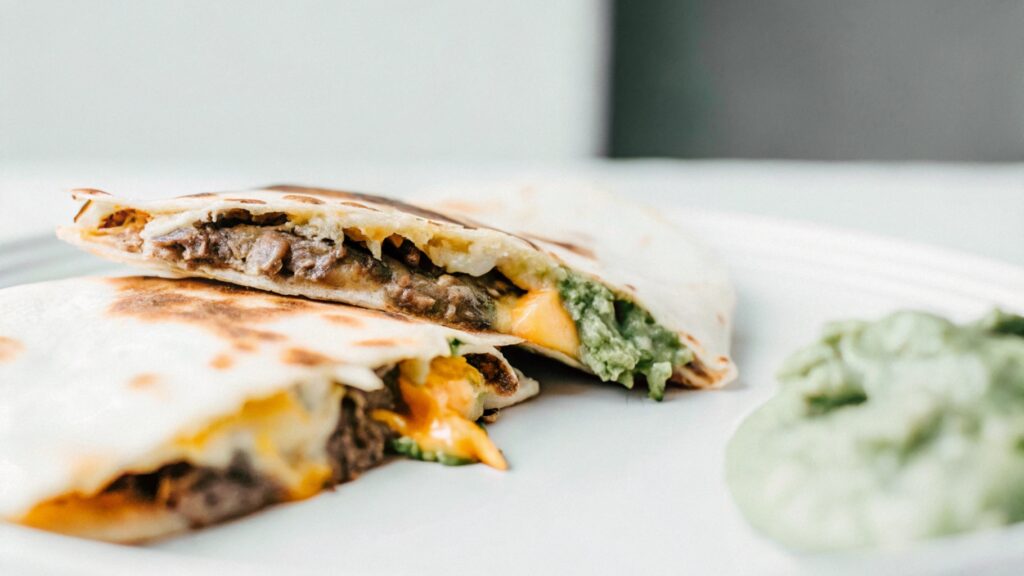 A close-up of hands pulling apart a quesadilla, showing stretchy Oaxaca cheese between the crispy tortilla halves.