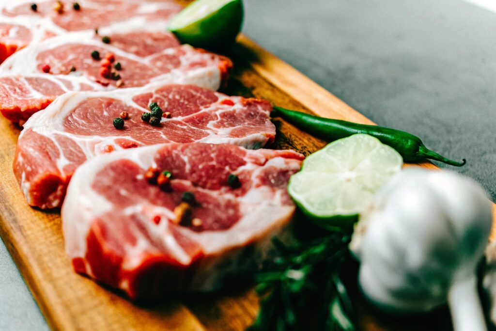 Fresh steak cuts, chipotle peppers in adobo sauce, garlic cloves, lime, and an assortment of spices arranged on a rustic wooden cutting board