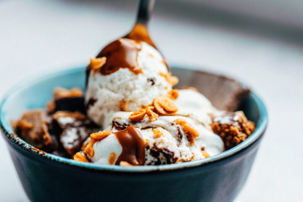 Close-up of freshly churned banana pudding ice cream being scooped into a bowl, topped with crushed vanilla wafers and caramel drizzle.